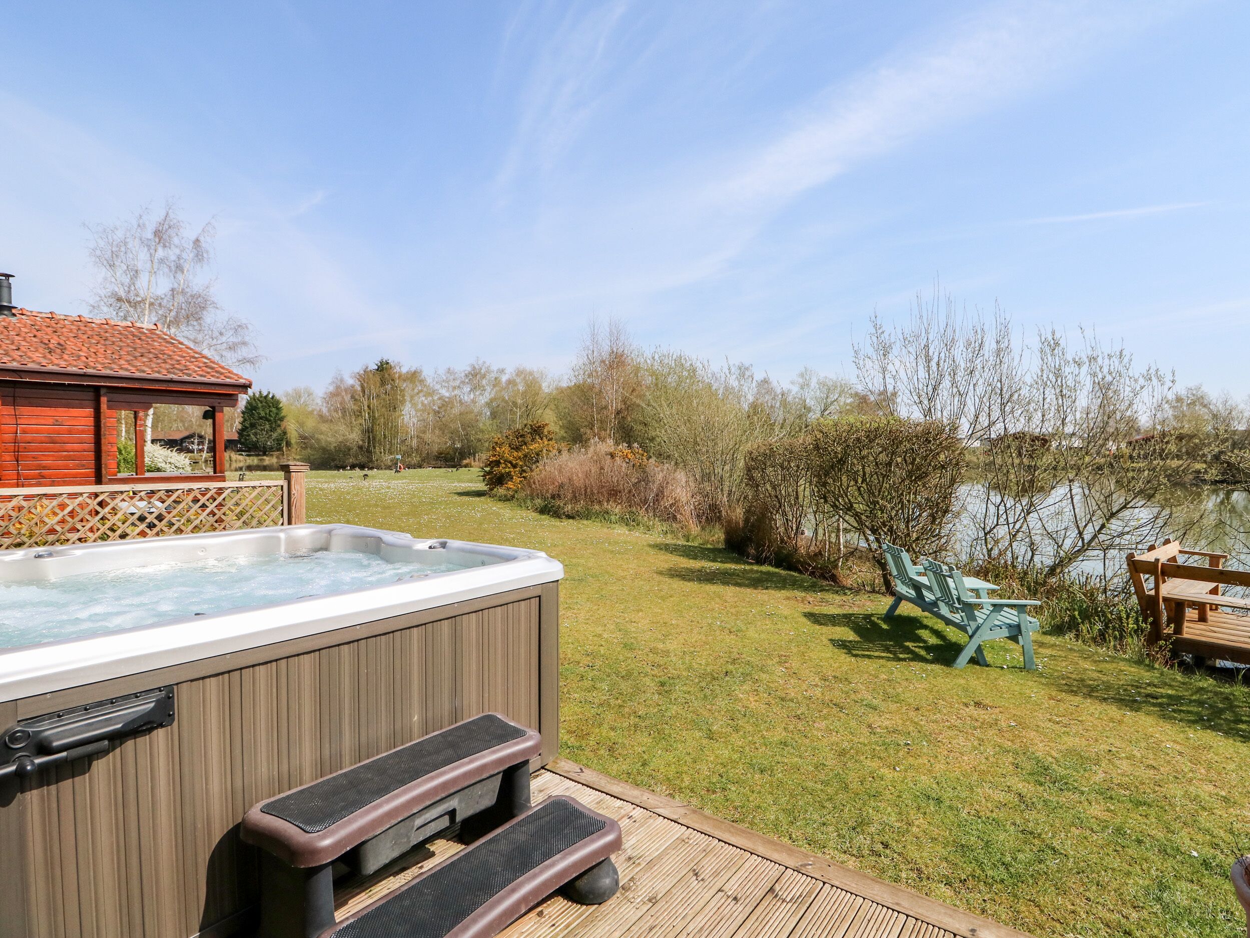 Een hottub met treden, een houten terras en uitzicht op een meer met bomen en een houten constructie op de achtergrond.