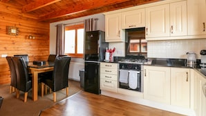 Un interior de madera con comedor, cocina y un ventanal con cortinas.