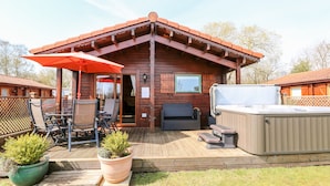 Una cabaña de madera con un patio amoblado, que incluye muebles de exterior, un jacuzzi y plantas en macetas.