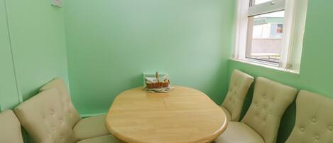 Un coin repas avec une table ronde en bois, entourée de quatre chaises beiges à revêtement rembourré. Un panier contenant divers objets est posé sur la table.
