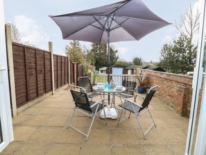 A patio with a table and chairs, a large umbrella, and a brick wall. - 7 Coastal Cottages (Lowestoft)
