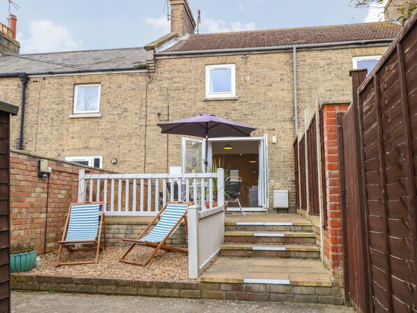 A brick house with a small patio area featuring two striped lounge chairs and a purple umbrella. - 7 Coastal Cottages (Lowestoft)