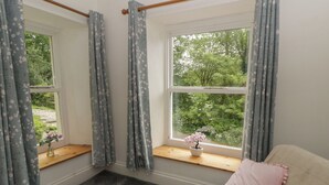 A bedroom with a large window, a small table with a vase, and a bed with pink pillows. - Teifi House (Cardigan)