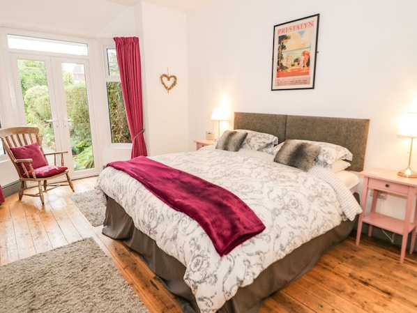 A bedroom with a large bed, two bedside tables, a rocking chair, and a window with curtains. - Hafan Y Mor (Colwyn Bay)