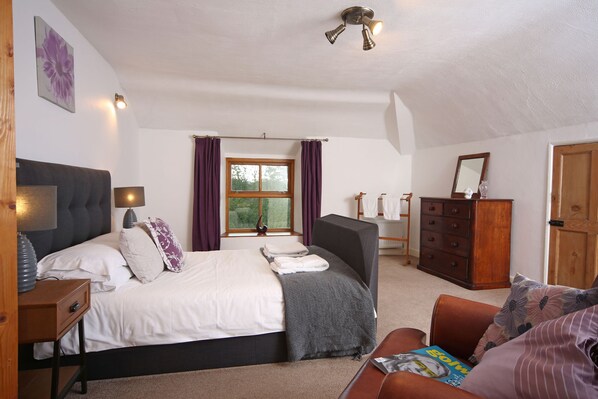 A bedroom with a bed, bedside table, dresser, and a window with curtains. - Tywysog (Denbigh)