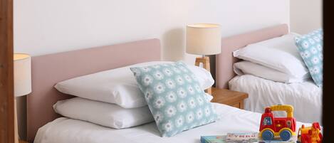 A neatly made bed with white bedding and a blue floral pillow, a small bedside table with a lamp, and a toy fire truck on the bed.