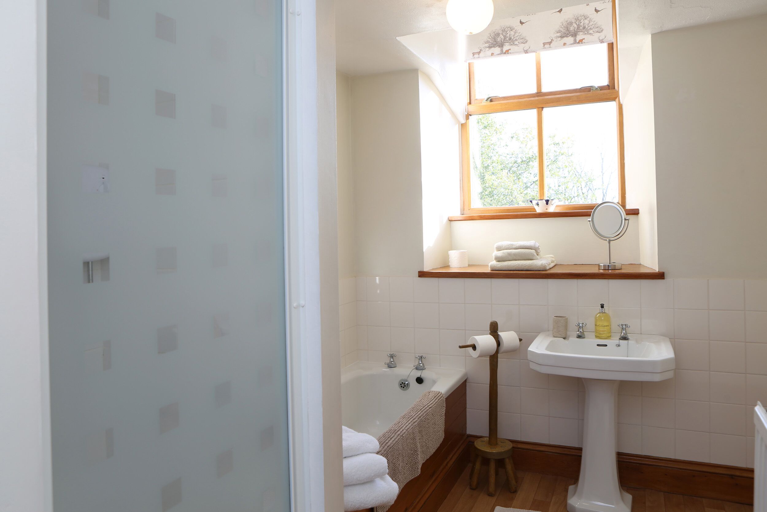 Un baño con bañera, lavamanos, ventana con vistas y espejo.