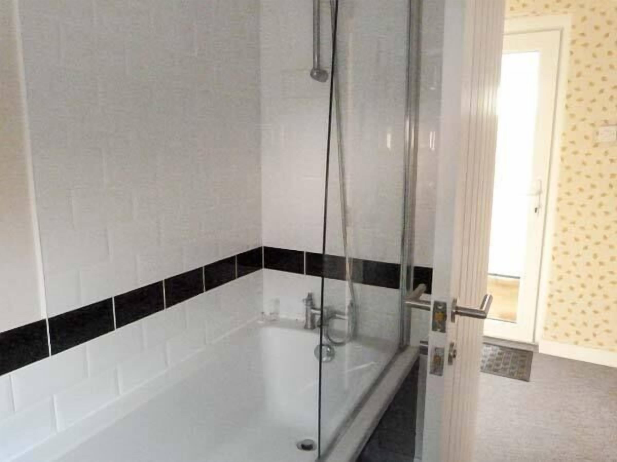 A bathroom with a glass-enclosed shower, white tiled walls, and a black tile accent strip.