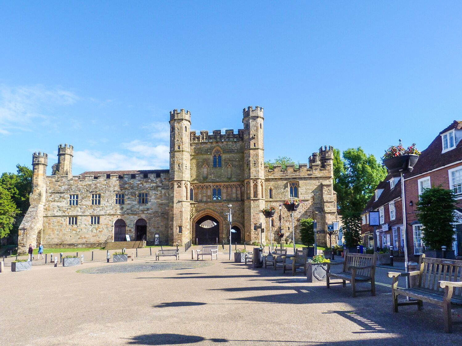 A historic stone building with a central tower and arched entrance, surrounded by benches and a paved area.