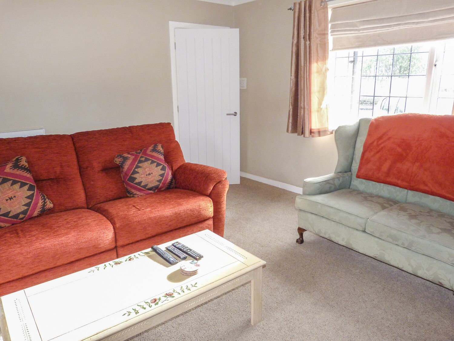 A living room with a red sofa, a light grey armchair, and a white coffee table with remote controls.