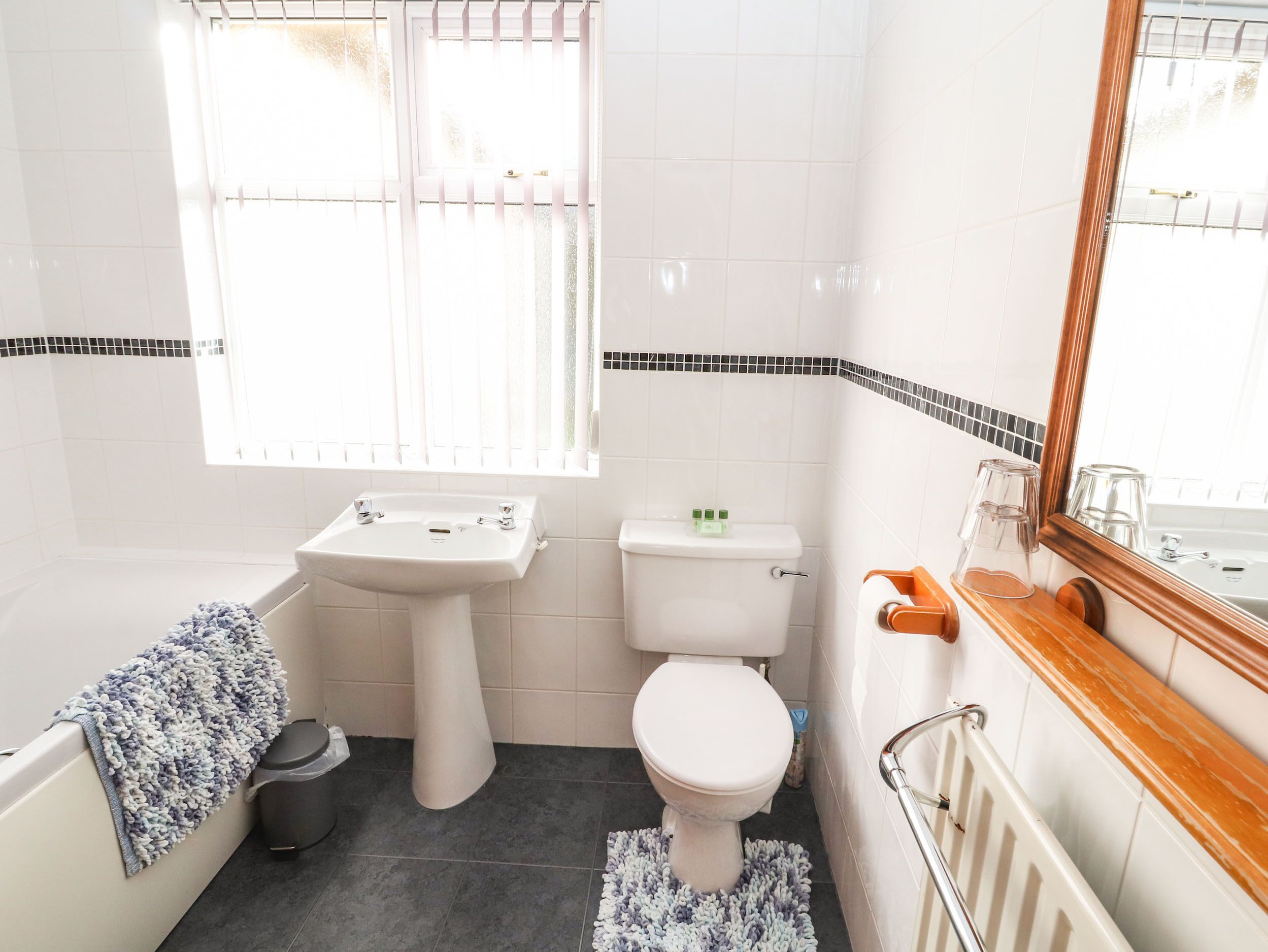 A bathroom with a bathtub, sink, toilet, and a window with blinds.