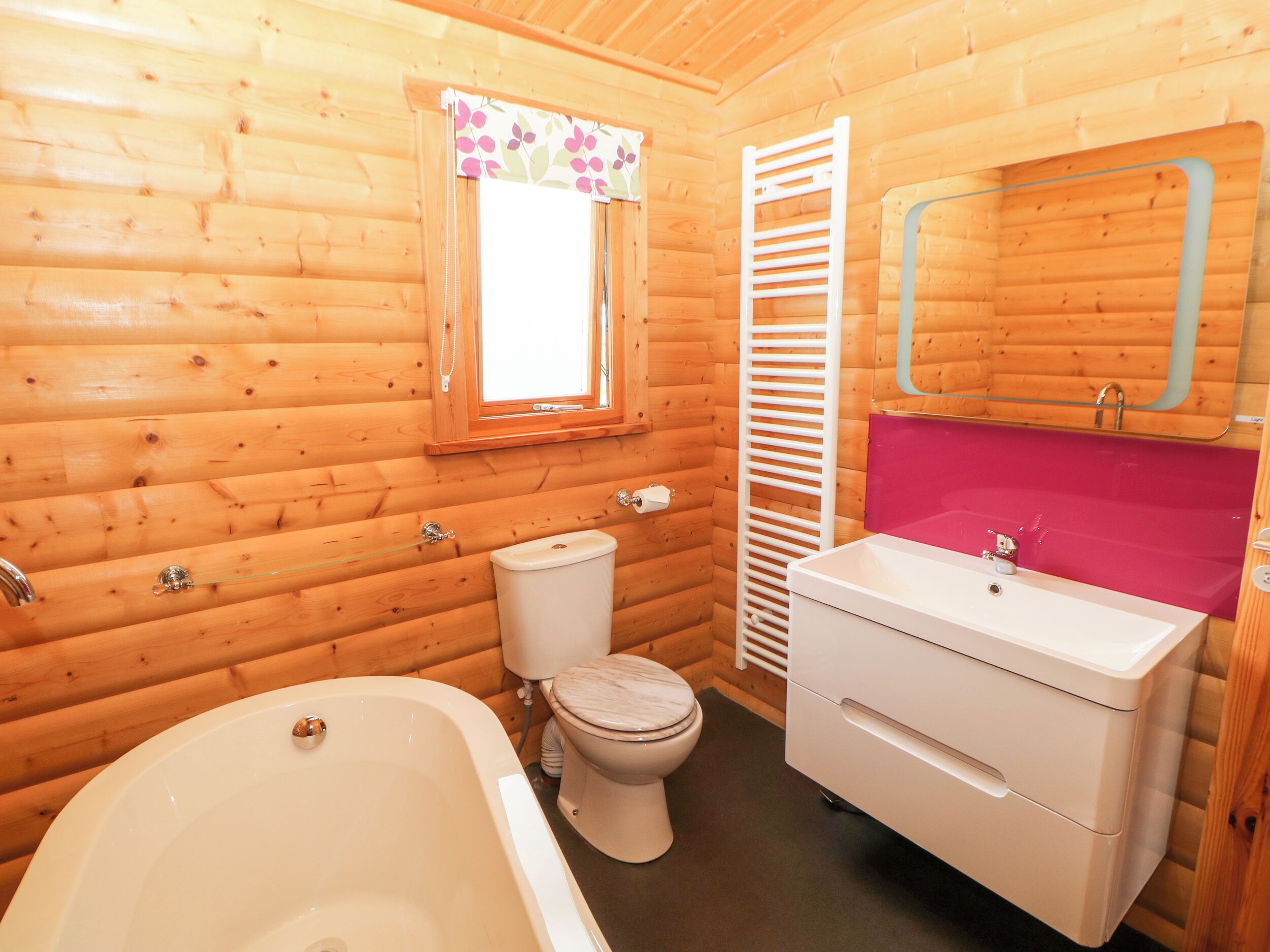 A wooden cabin bathroom with a bathtub, toilet, and a vanity with a mirror.