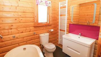 A wooden cabin bathroom with a bathtub, toilet, and a vanity with a mirror.