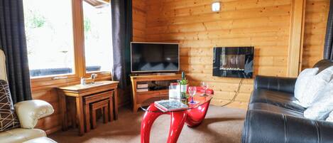 A cozy cabin interior with a wooden interior, a TV, a dining table with chairs, and a sofa.