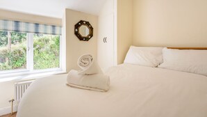 A neatly made bed with white linens, a rolled towel, and a decorative mirror on the wall. - Kynaston Cottage (Aberdovey)