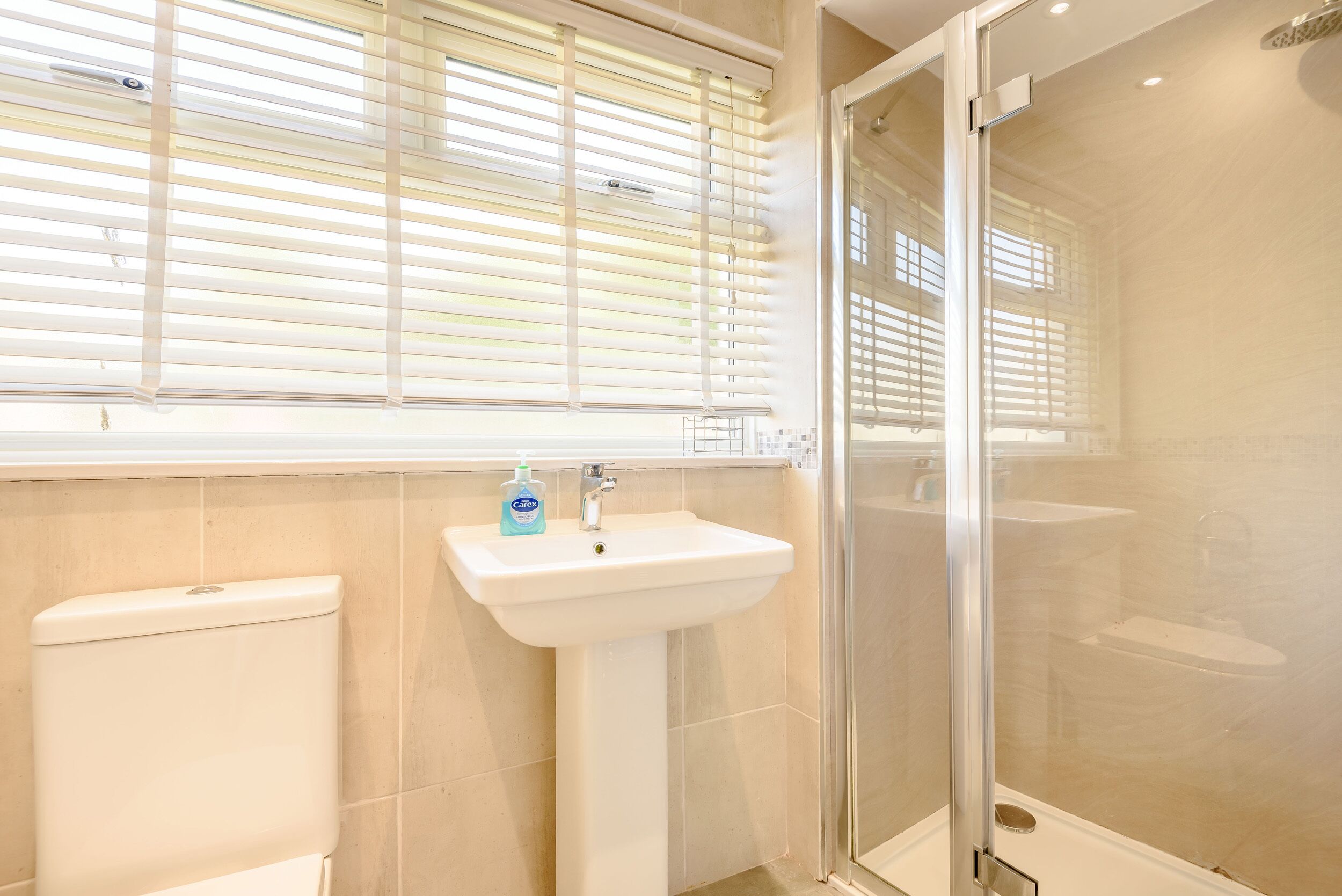 A bathroom with a toilet, sink, and glass shower enclosure.