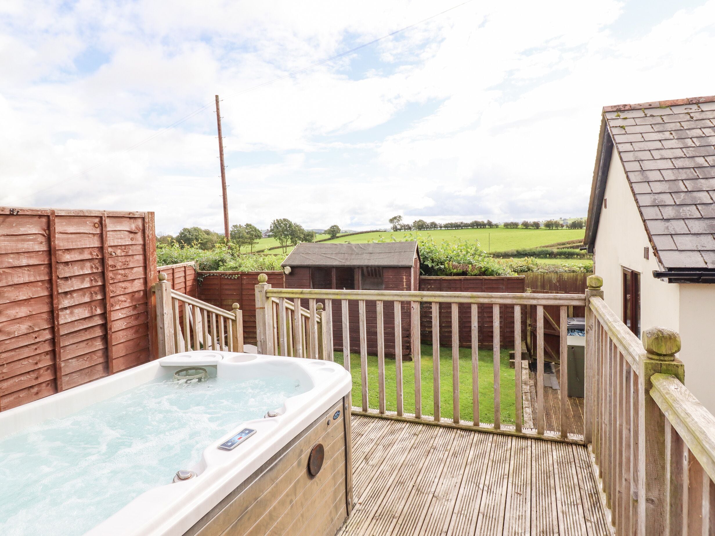 A hot tub in a wooden deck area with a view of a green field and a small building in the background.