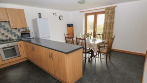 Una cocina con armarios de madera, encimera negra, estufa y microondas. Hay una mesa de comedor con sillas y una ventana con cortinas.