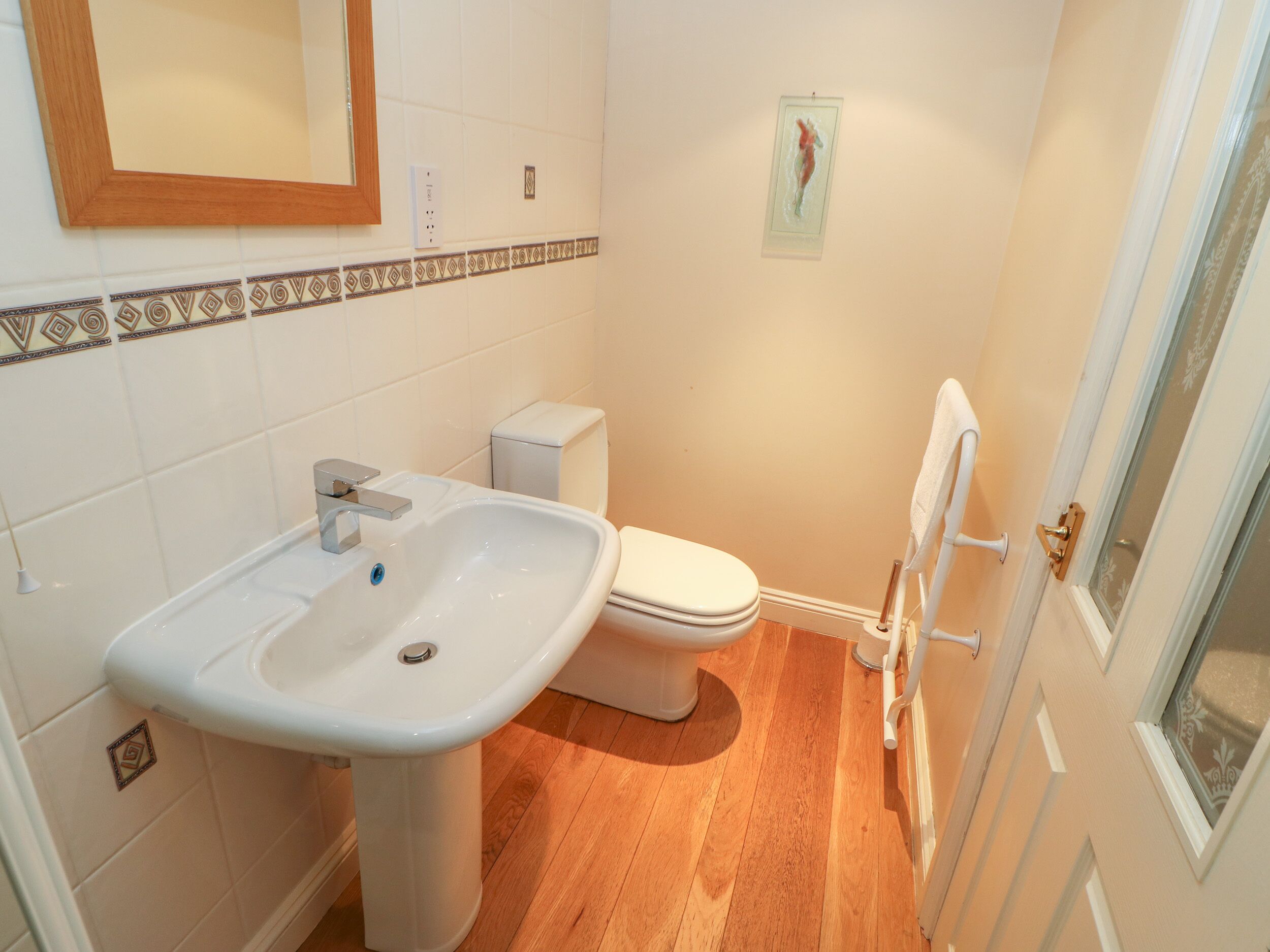 Une salle de bain avec un lavabo blanc, des toilettes et un plancher en bois.