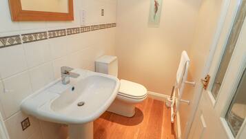 Une salle de bain avec un lavabo blanc, des toilettes et un plancher en bois.