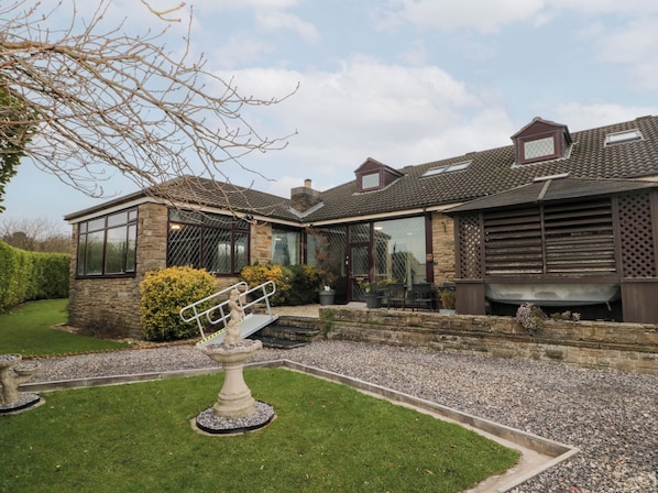 A stone house with a large glass window, a patio with outdoor furniture, and a garden with a birdbath.