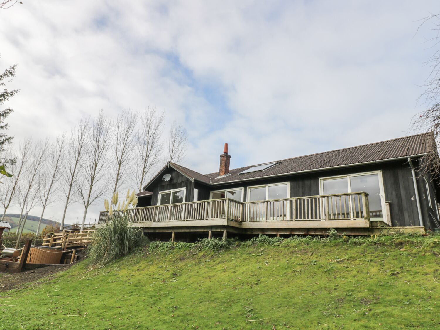 A two-story wooden house with a balcony, a chimney, and a grassy hill in the foreground.