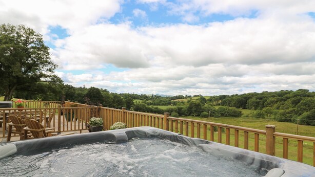 A hot tub on a wooden deck with a view of a green landscape. - Foxes Meadow (Llandrindod Wells)