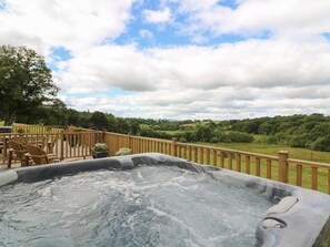 A hot tub on a wooden deck with a view of a green landscape.