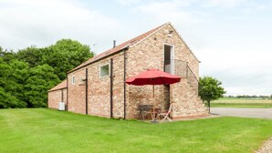 A brick building with a red umbrella, a small outdoor seating area, and a grassy lawn. - The Stables, Crayke Lodge (York)
