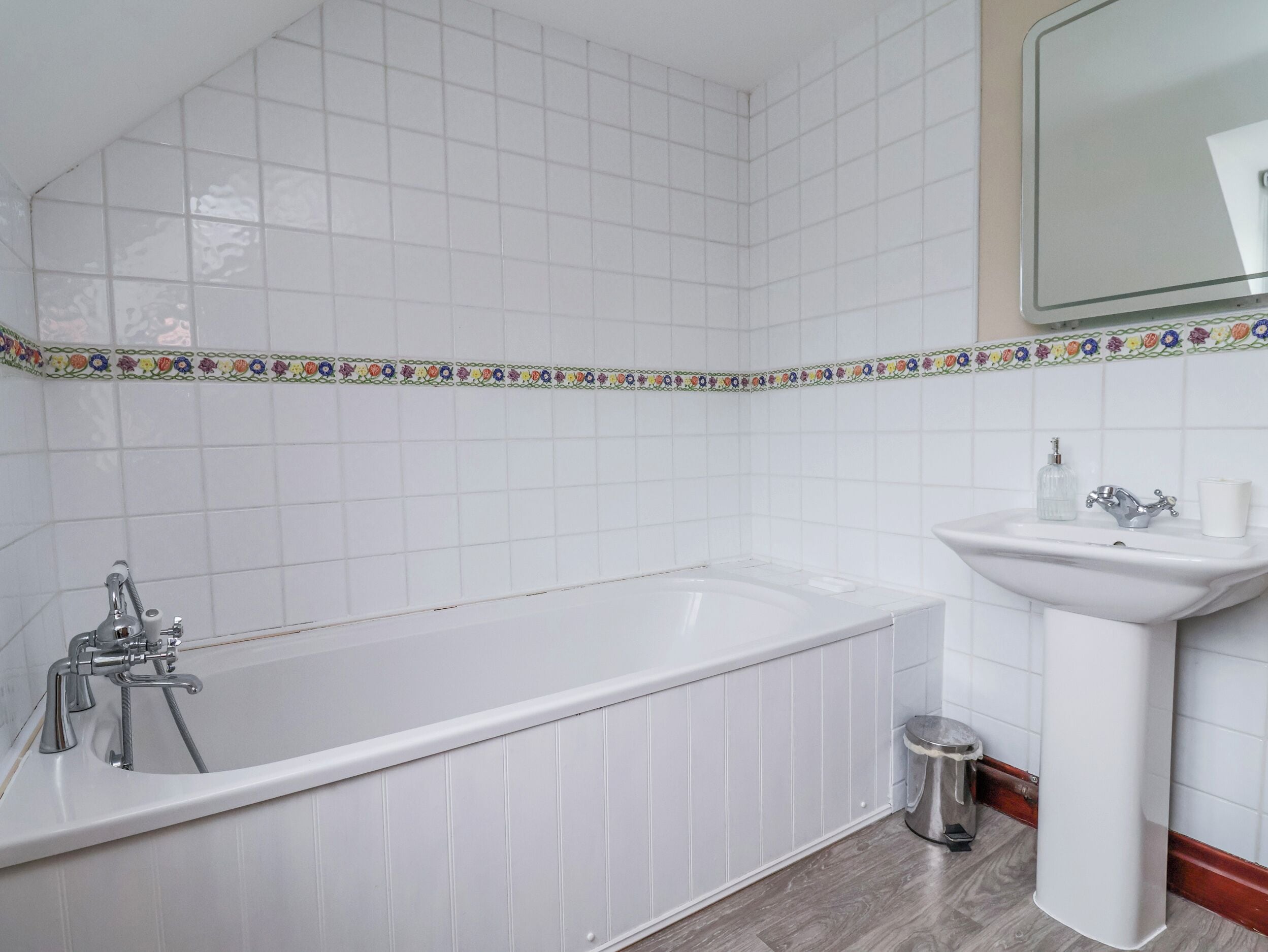A bathroom with a white bathtub, a sink, and a trash bin.