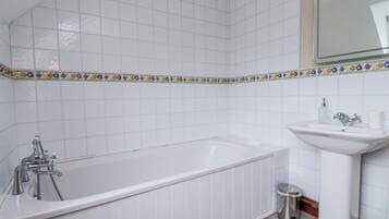 A bathroom with a white bathtub, a sink, and a trash bin.