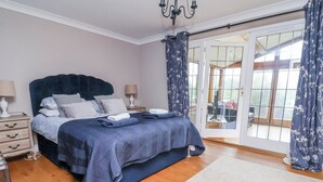 Une chambre à coucher avec un lit, des tables de chevet, un lustre et une vue sur l’extérieur, visible à travers une porte vitrée.