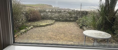 A stone pathway leading to a stone wall, with a small table and a palm tree visible.