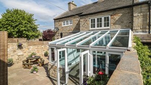 A stone house with a glass conservatory, stone patio, and potted plants. - Belgrave House (Barnard Castle)