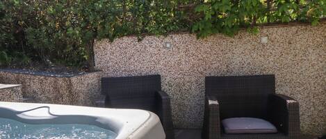 A hot tub with two wicker chairs and a stone wall.