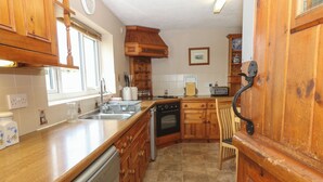 A kitchen with wooden cabinets, a dishwasher, an oven, and a sink. - Porth Awyr (Pwllheli)