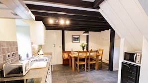 A modern kitchen with a built-in oven, a microwave, and a sink. There is a dining area with a table and chairs. - Hen Gelligemlyn - The Annexe (Dolgellau)
