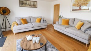 A modern living room with two grey sofas, a round wooden coffee table, and a floor lamp. - Pheasant Wood (Llandrindod Wells)