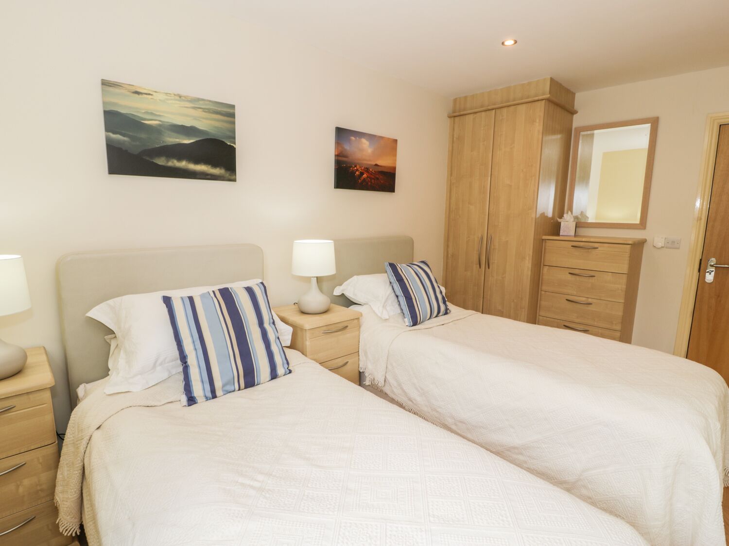 A double room with two beds, a wooden wardrobe, a mirror, and two wall-mounted paintings.