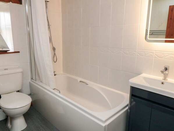 A bathroom with a white bathtub, a toilet, and a sink. - Goathland Cottage (Whitby)
