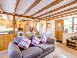 A cozy living room with a sofa, a dining table, and a kitchen area with wooden beams and a washing machine. - Goathland Cottage (Whitby)