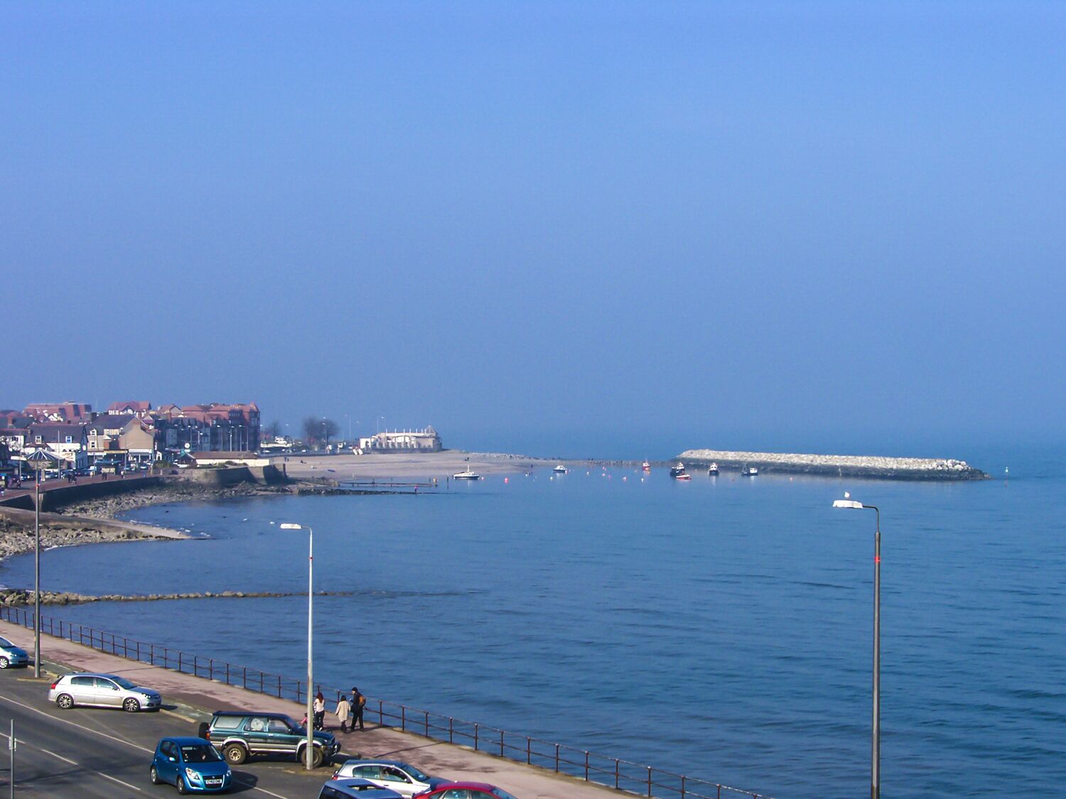 A coastal road with parked cars and a pedestrian walkway alongside the sea.