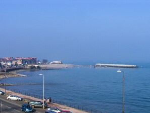 A coastal road with parked cars and a pedestrian walkway alongside the sea. - Roma (Colwyn Bay)
