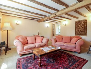 A living room with two pink sofas, a wooden coffee table, a patterned rug, exposed wooden beams, and a wall-mounted tapestry. - Just A Cottage, Newlands Farm (Alfreton)