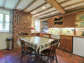 A kitchen with a brick wall, wooden cabinets, a tiled backsplash, and a dining table with chairs. - Just A Cottage, Newlands Farm (Alfreton)