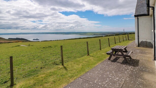 A grassy field with a picnic table and a building with a view of a body of water. - Little Laight (Stranraer)