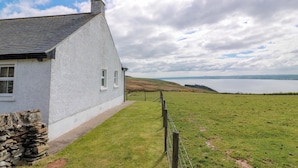 A white house with a stone wall, a grassy field, and a view of the sea. - Little Laight (Stranraer)