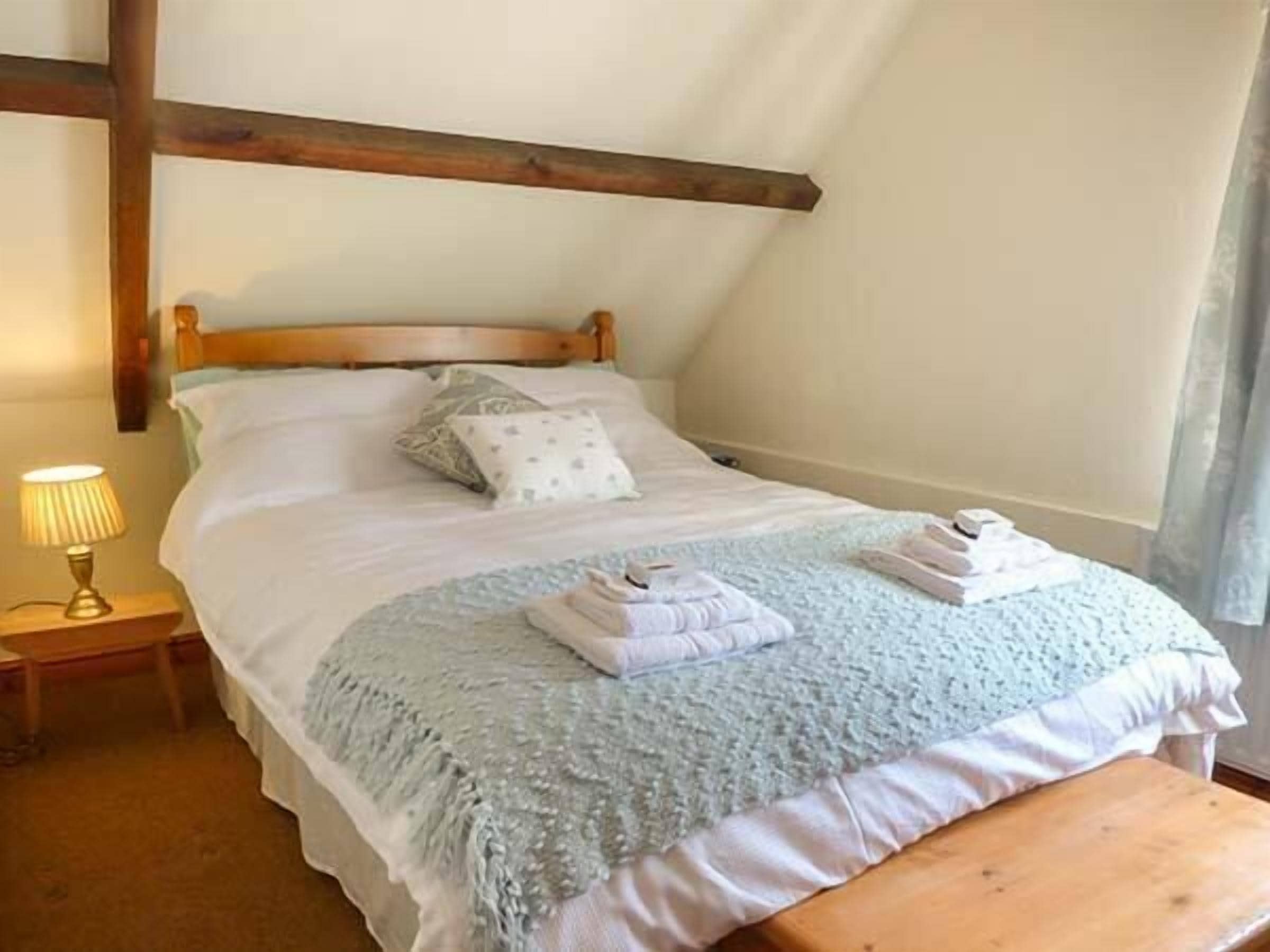 A neatly made bed with a blue blanket and pillows, a bedside lamp, and a wooden bench.