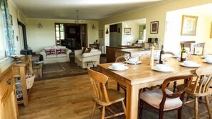 Un comedor con una mesa de madera dispuesta para cuatro personas, rodeada de sillas de madera. Se observa una cocina al fondo, con un refrigerador y un microondas.