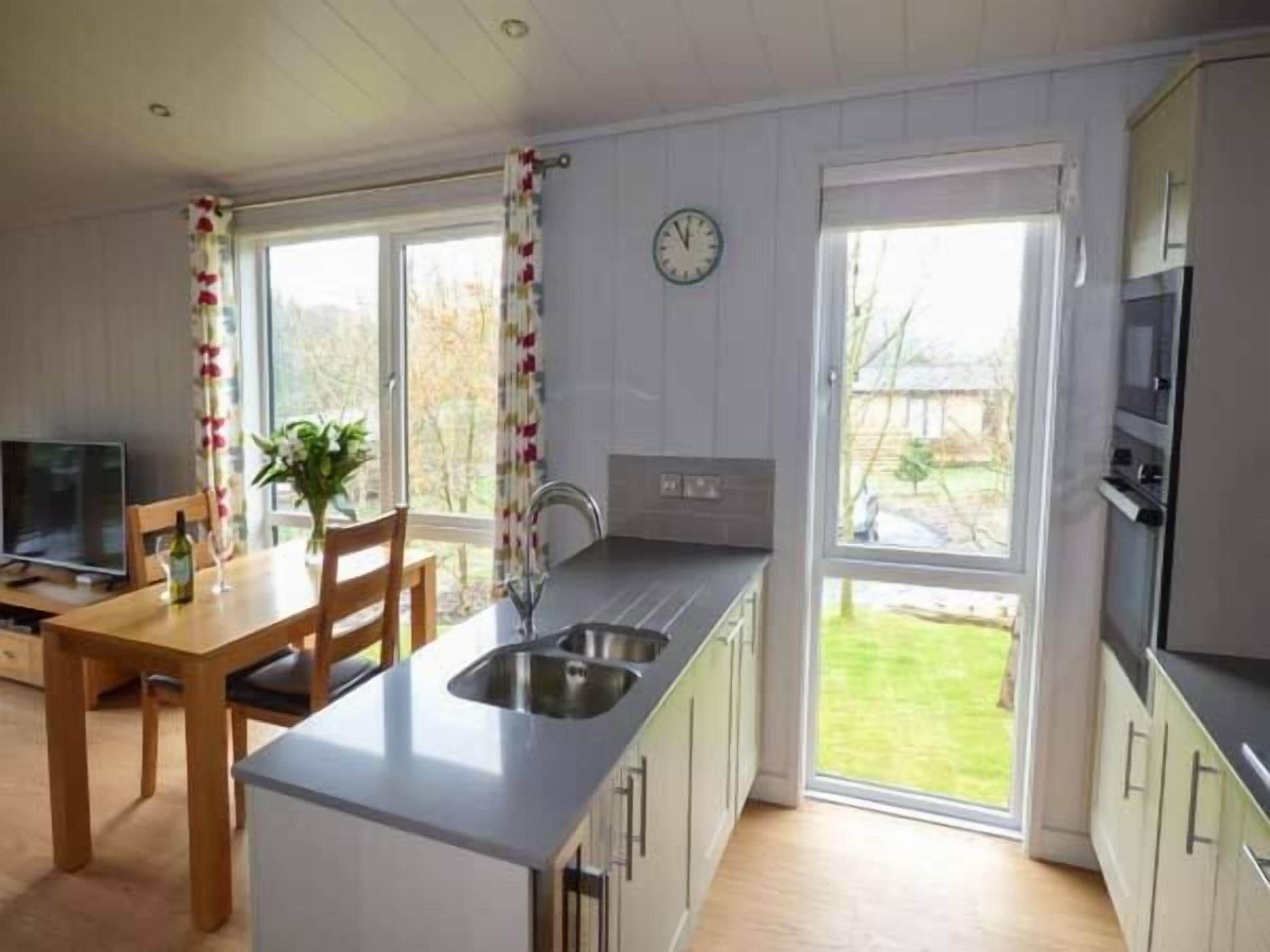 A modern kitchen with a dining area, large windows, and a clock on the wall.